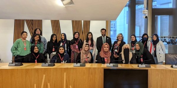A group of diverse young Muslim women standing around former FM Humza Yousaf and MSP Kaukab Stewart inside Scottish Parliament